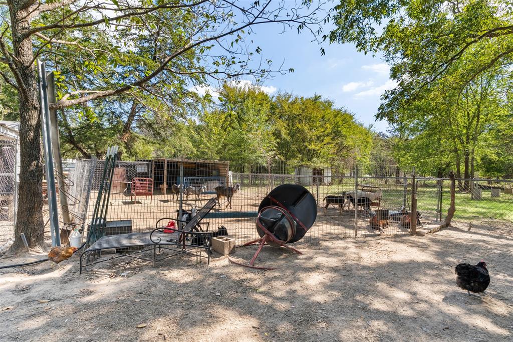 Fenced exterior area featuring mature trees and a covered livestock structure