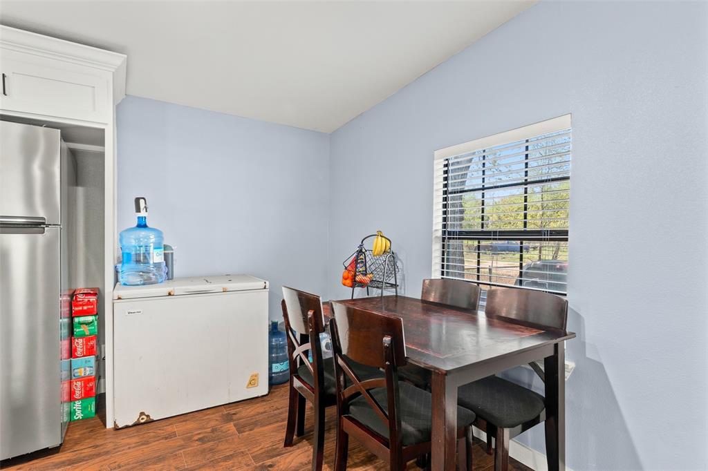 Kitchen area featuring wood-finish flooring, white cabinetry, stainless steel refrigerator, and a window with horizontal blinds
