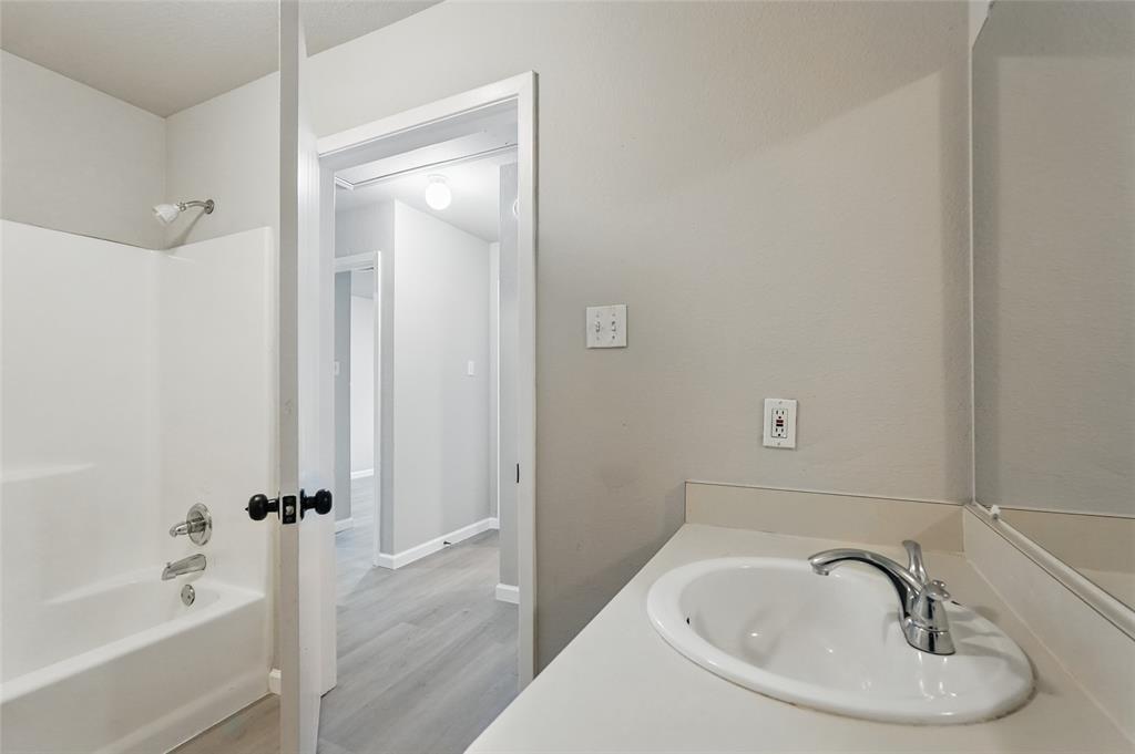 Bathroom featuring a tub-shower combination with integrated surround, vanity with an integrated basin, chrome-finish faucet, and wood-finish flooring