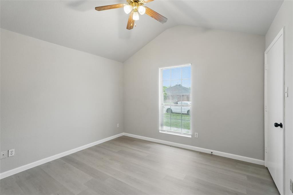 Vaulted ceiling, neutral wall tones, wood-finish flooring, single-pane window with grid pattern, and ceiling fan with integrated light fixture