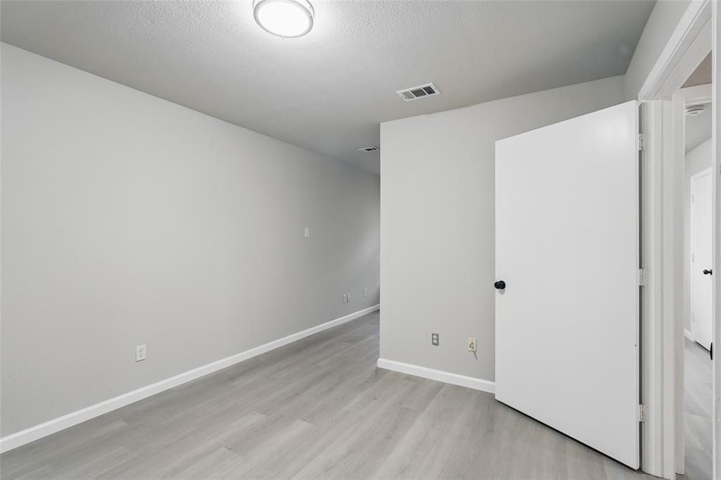 Neutral-toned room featuring wood-finish flooring, a white interior door, and a flush-mount overhead light fixture