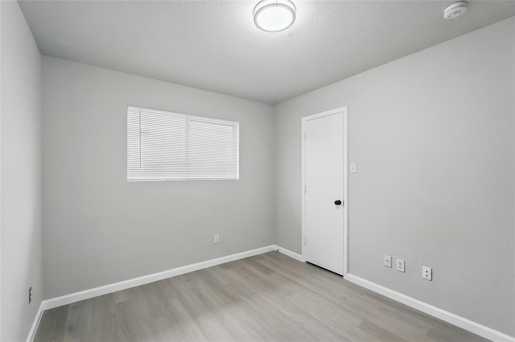 Neutral-toned room featuring wood-finish flooring, a single-panel interior door with a matte black handle, a horizontal window with adjustable blinds, and a flush-mount dome light fixture