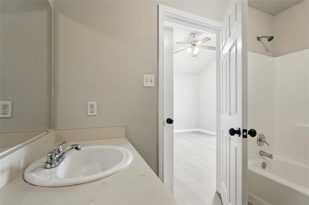 Bathroom featuring a vanity with a white integrated sink, a large wall-mounted mirror, a tub-shower combination, and a six-panel door with black hardware