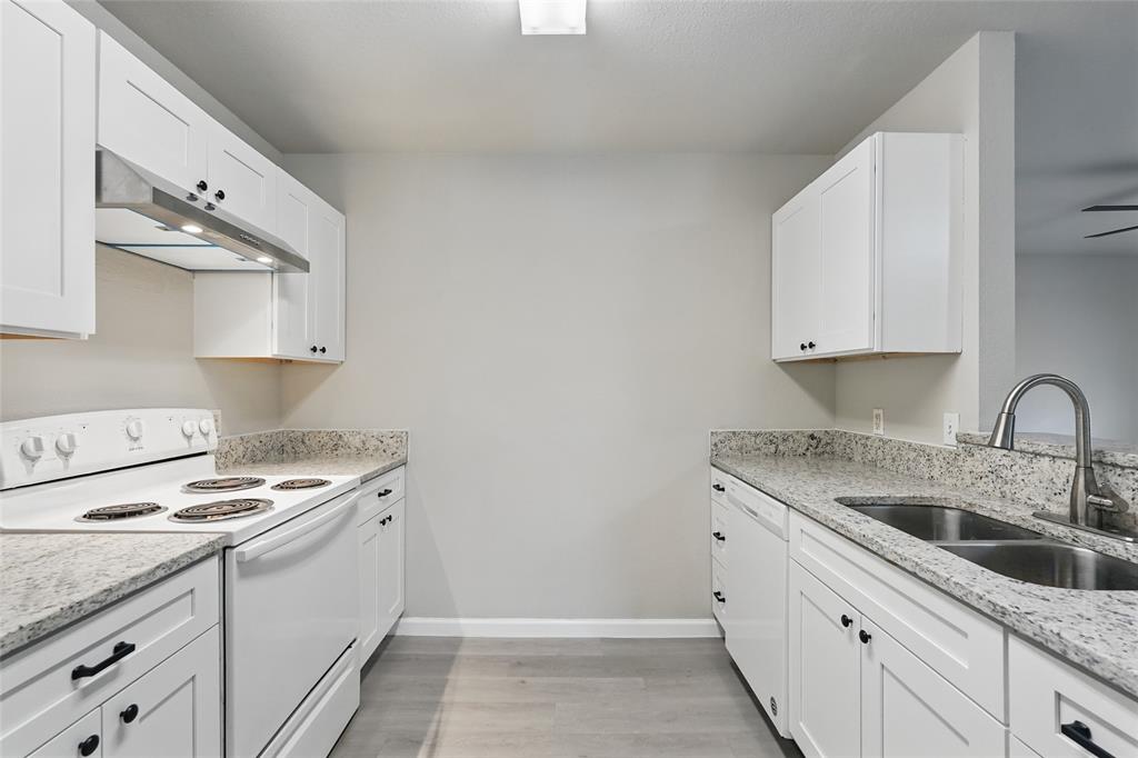 Kitchen featuring white shaker-style cabinetry, stone-finish countertops, stainless steel dual-basin sink with arched faucet, overhead range hood, and wood-finish flooring
