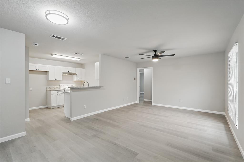 Open-concept living space featuring wood-finish flooring, white shaker-style cabinetry, a stone-surface breakfast bar, a ceiling fan with integrated lighting, and flush-mount overhead illumination