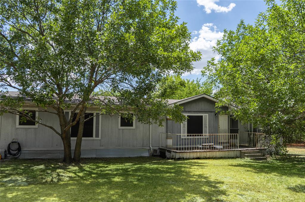 Exterior facade with neutral siding, raised deck featuring metal railings, and mature trees situated on a grassy lot