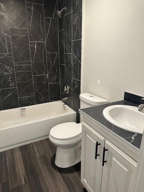 Bathroom featuring vertical dark stone-finish tile shower surround, white cabinetry, dark stone-finish countertop with integrated sink, and wood-finish flooring