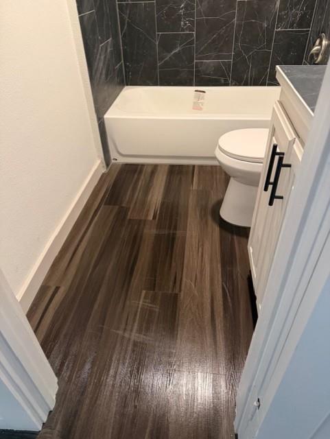 Bathroom featuring wood-finish flooring, dark stone-patterned tile shower surround, and vanity with dark hardware