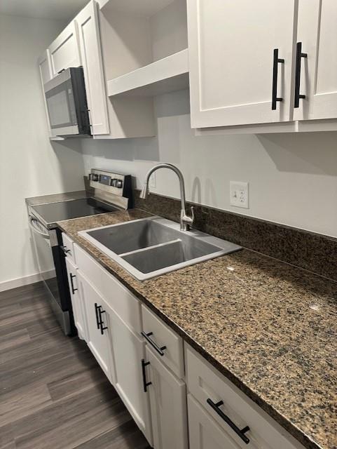 Kitchen featuring white shaker-style cabinetry with matte black hardware, stone-patterned countertops, stainless steel dual-basin sink with gooseneck faucet, integrated stainless steel microwave, and wood-finish flooring