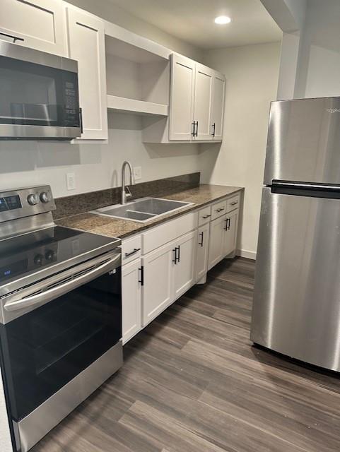 Kitchen featuring white cabinetry with matte black hardware, stainless steel appliances, stone-surface countertops, dual-basin stainless steel sink, and wood-finish flooring