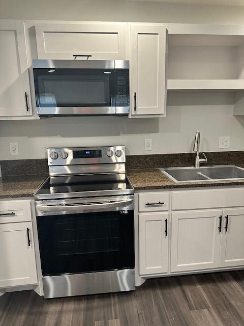 Kitchen featuring white cabinetry with matte black hardware, stainless steel electric range, over-the-range microwave, dark stone-finish countertops, and dual-basin sink with arched faucet