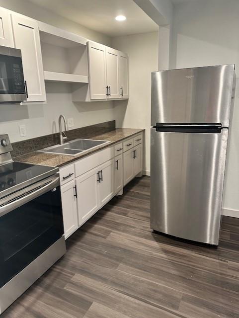 Kitchen featuring white shaker-style cabinetry, stainless steel appliances, dark stone-finish countertops, stainless steel dual-basin sink with arched faucet, and wood-finish flooring