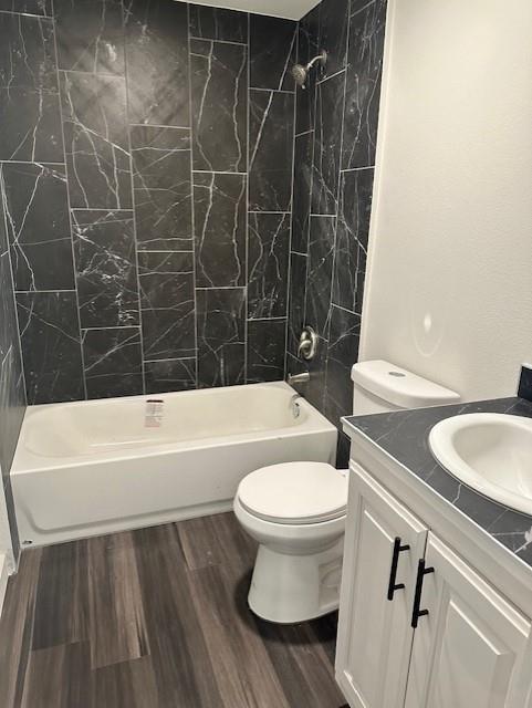 Bathroom featuring floor-to-ceiling dark stone-finish wall tile, white vanity with black hardware, integrated sink with stone-finish countertop, and wood-finish flooring