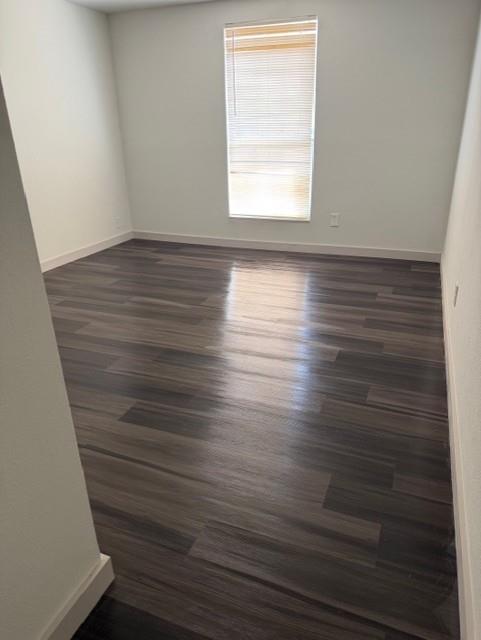 Room featuring wood-finish flooring, neutral walls, and a single vertical window with installed blinds