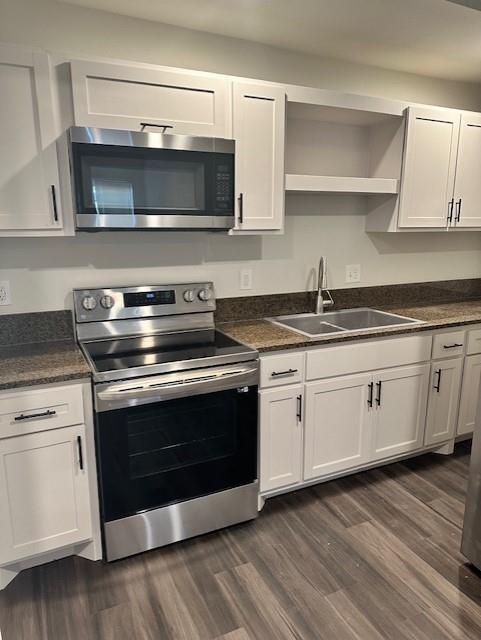 Kitchen featuring white shaker-style cabinetry, stainless steel appliances, dark stone-finish countertops, integrated microwave, and wood-finish flooring