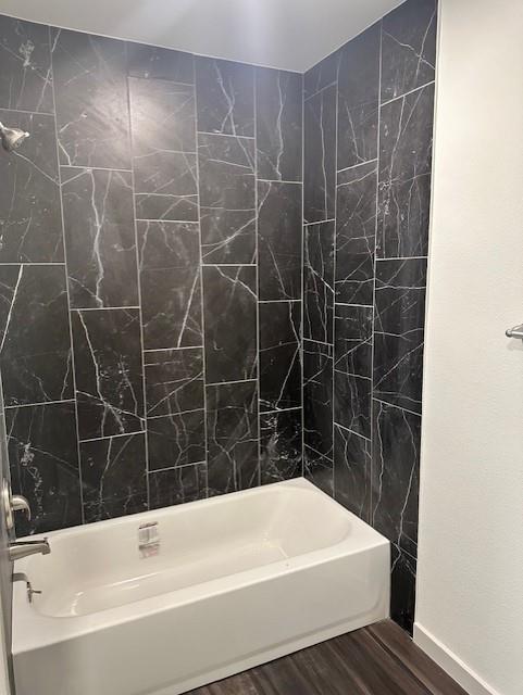 Bathtub surround featuring large-format, dark stone-finish tile with white veining, polished chrome faucet, and integrated shower head