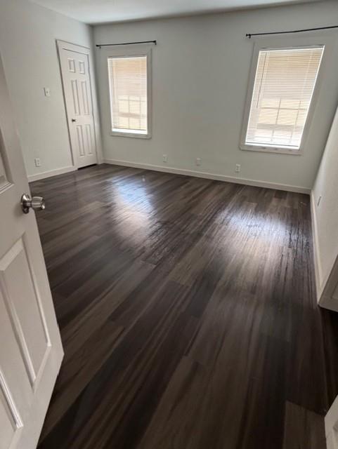 Neutral interior space featuring wood-finish flooring, two windows with horizontal blinds, and a paneled door