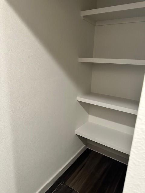 Built-in closet featuring three tiers of fixed white shelving and dark wood-finish flooring