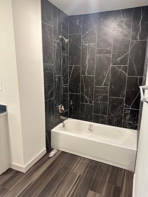 Bathroom featuring a white bathtub, full-height wall surround with large-format dark patterned tile, and wood-finish flooring