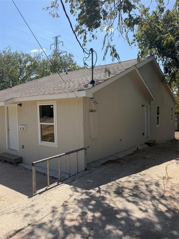 Exterior featuring vertical siding, a gable roof with asphalt shingles, and concrete pavement