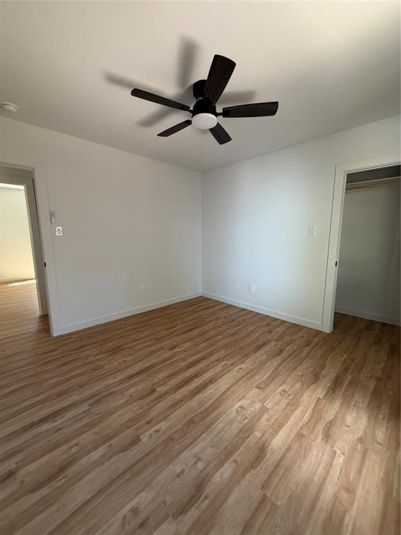 Neutral interior featuring wood-finish flooring, white walls, and a five-blade ceiling fan with integrated lighting