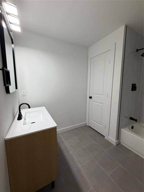 Bathroom featuring a wood-finish vanity with a rectangular sink, quartz countertop, matte black fixtures, and large-format tile flooring