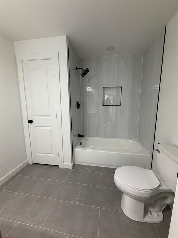 Bathroom featuring oversized grey floor tiling, a tub-shower combination with vertical wall tile, an integrated recessed shower niche, and matte black plumbing fixtures