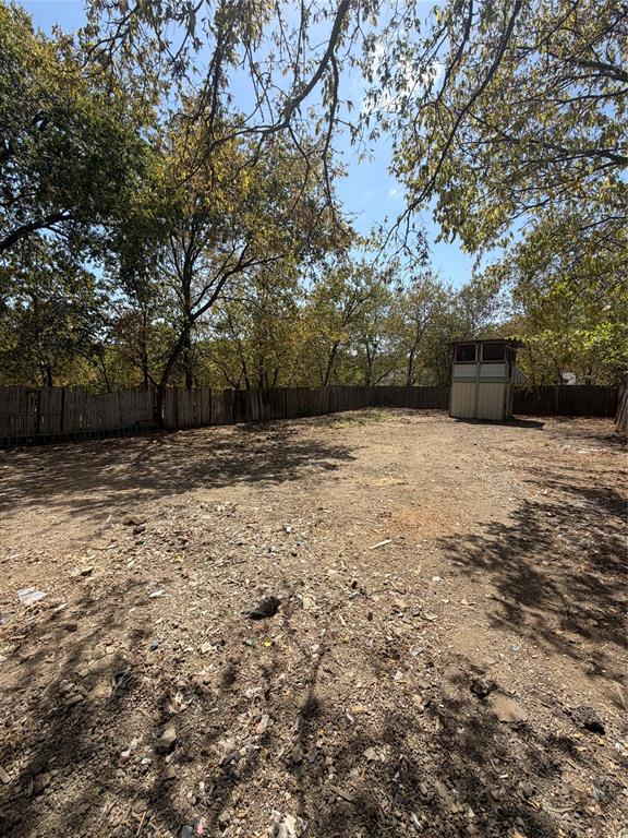 Open outdoor area enclosed by a wood-slat perimeter fence with mature trees and a detached storage structure