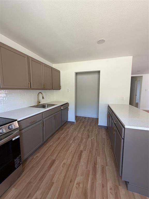 Kitchen featuring shaker-style cabinetry, white countertops, a subway tile backsplash, a stainless steel undermount sink with a high-arch faucet, and wood-finish flooring