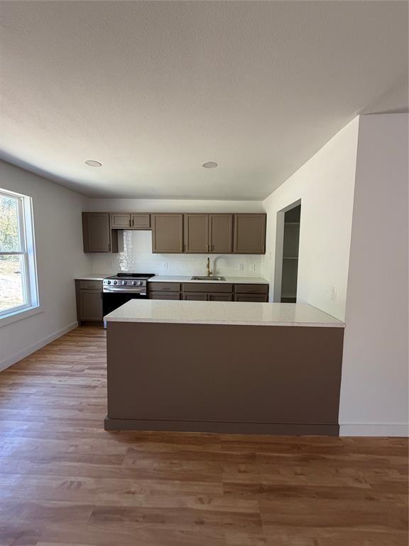 Kitchen featuring an island with a light-toned countertop, wood-finish cabinetry, stainless steel range, light-toned backsplash, and wood-finish flooring