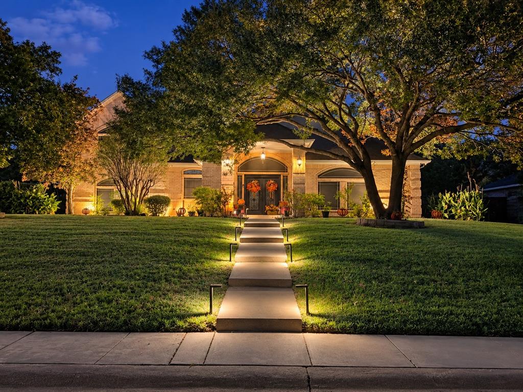 Masonry exterior featuring an arched entryway, stone facade, concrete walkway, and mature landscape trees