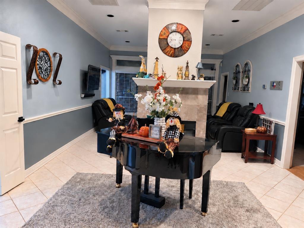 Living space featuring a central fireplace with stone-tile surround, tile flooring, recessed lighting, crown molding, and chair rail wainscoting
