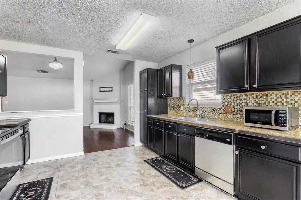 Kitchen featuring dark wood cabinetry, stone-finish countertops, decorative tile backsplash, stainless steel dishwasher, and tile flooring
