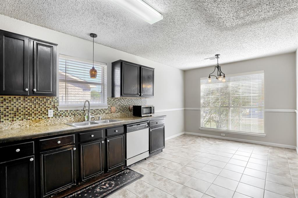 Kitchen featuring dark-finish cabinetry, stone-texture countertops, mosaic tile backsplash, integrated stainless steel dishwasher, and ceramic tile flooring