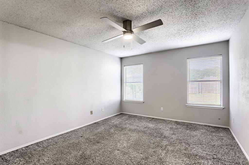 Room featuring neutral wall tones, gray carpeting, dual windows with fitted blinds, and a central ceiling fan with integrated lighting
