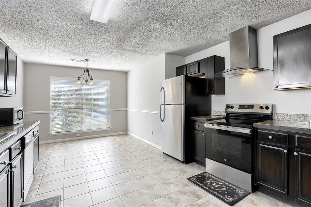 Kitchen featuring dark cabinetry, stone-finish countertops, a stainless steel range with a glass-canopy vent hood, and tile flooring
