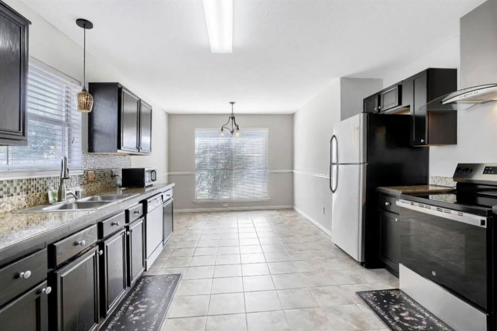 Kitchen featuring dark cabinetry, mosaic tile backsplash, stone-finish countertops, stainless steel appliances, and tile flooring