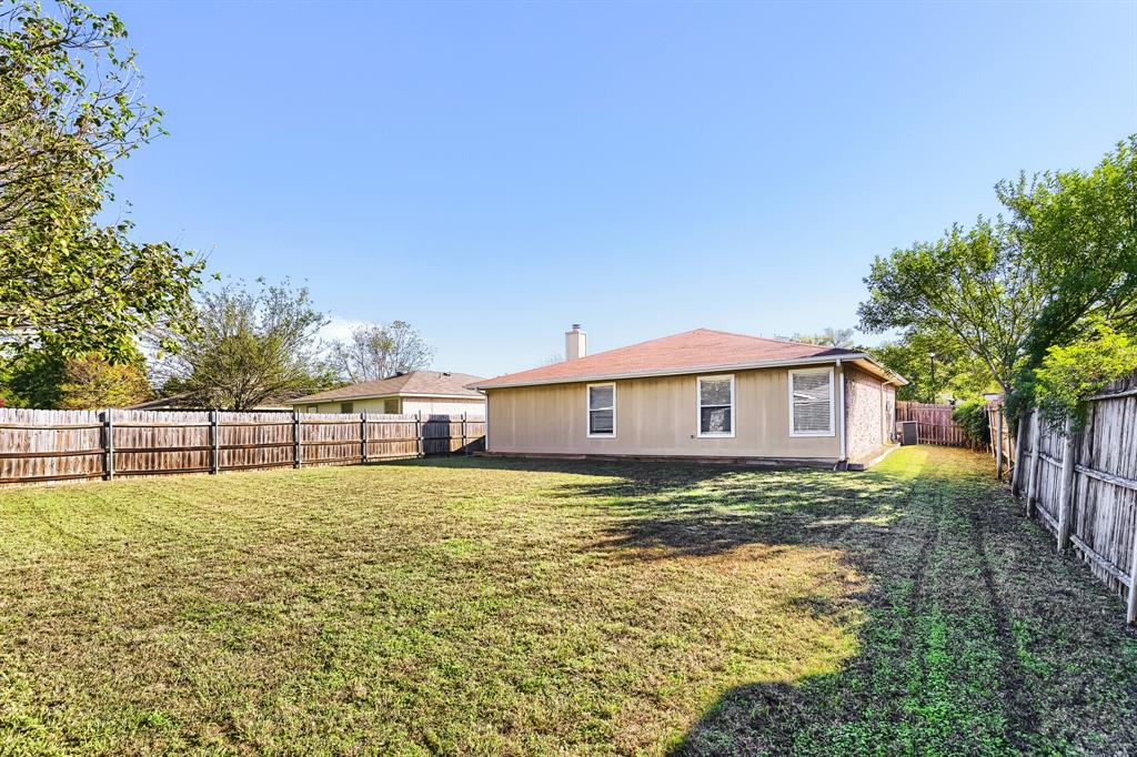 Spacious backyard featuring a grass lawn, perimeter wood fencing, and mature trees