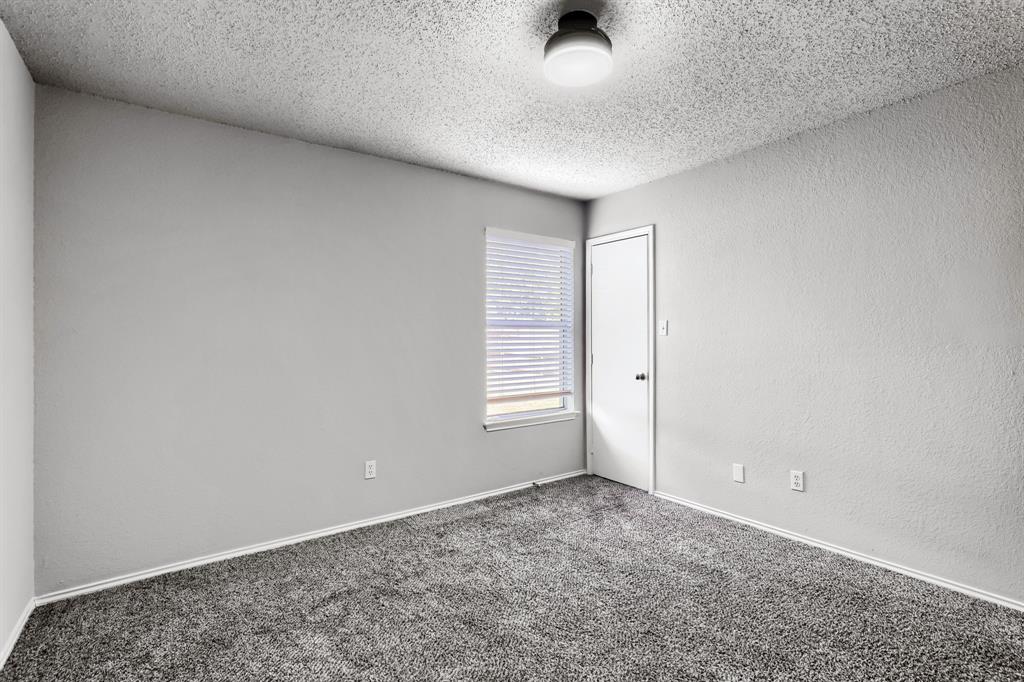 Neutral-toned carpeted flooring, textured ceiling, flush-mount light fixture, single-panel interior door, and window with white blinds