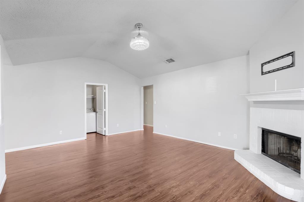Vaulted ceilings, wood-finish flooring, painted brick fireplace with a mantle, and a modern glass-cased ceiling light fixture