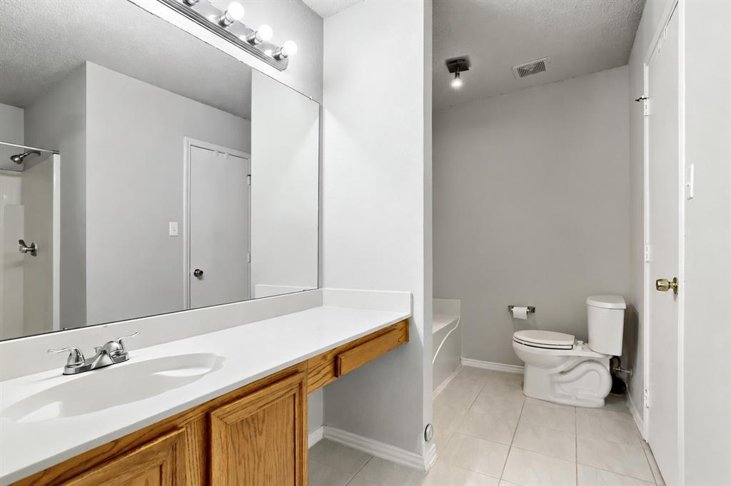Full-width vanity with integrated sink, wood-finish cabinetry, expansive wall-mounted mirror, ceramic tile flooring, and separate water closet area