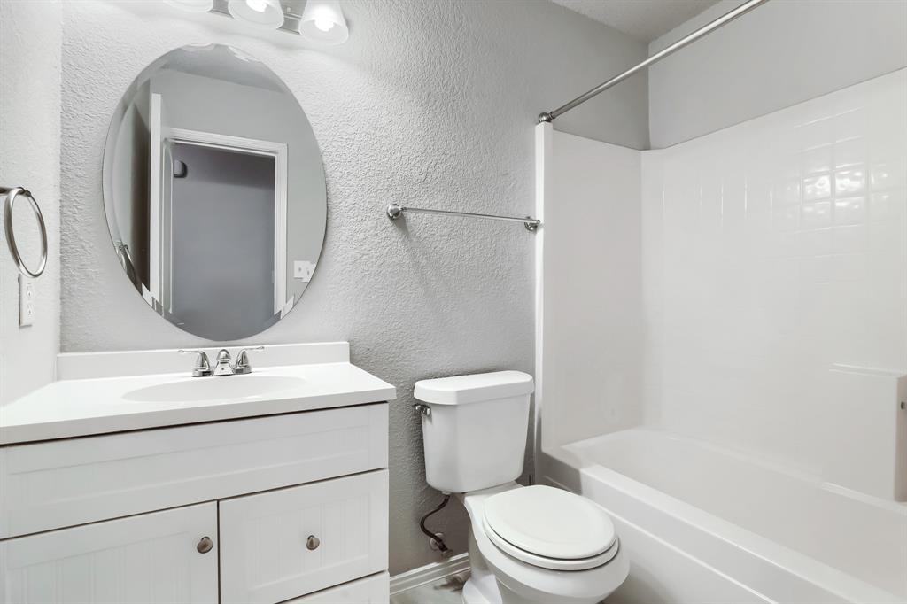 Bathroom featuring a white vanity with an integrated sink, oval wall-mounted mirror, three-light fixture, and a white tiled shower-tub combination