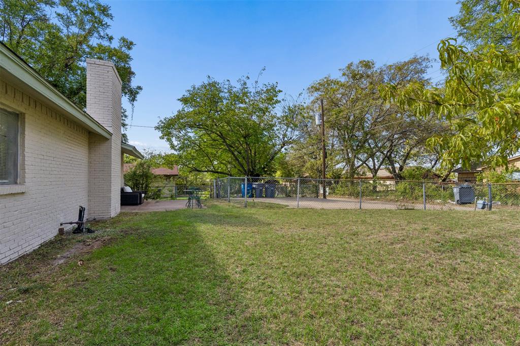 Backyard featuring a brick exterior wall, masonry chimney, chain-link perimeter fencing, and mature trees