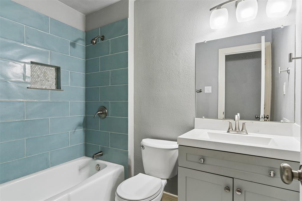Bathroom featuring a gray vanity with a white countertop, inset sink, large rectangular wall mirror, blue subway-tile shower surround with a built-in recessed niche, and three-light wall-mounted fixture