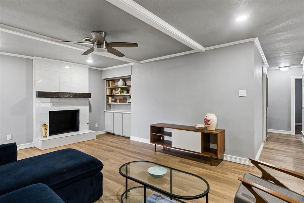 Fireplace with floor-to-ceiling surround, heavy timber mantel, recessed shelving, wood-finish flooring, and ceiling fan with integrated lighting