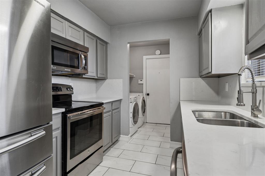 Kitchen featuring stainless steel appliances, grey cabinetry, solid-surface countertops, dual-basin sink with a high-arch faucet, and tile flooring