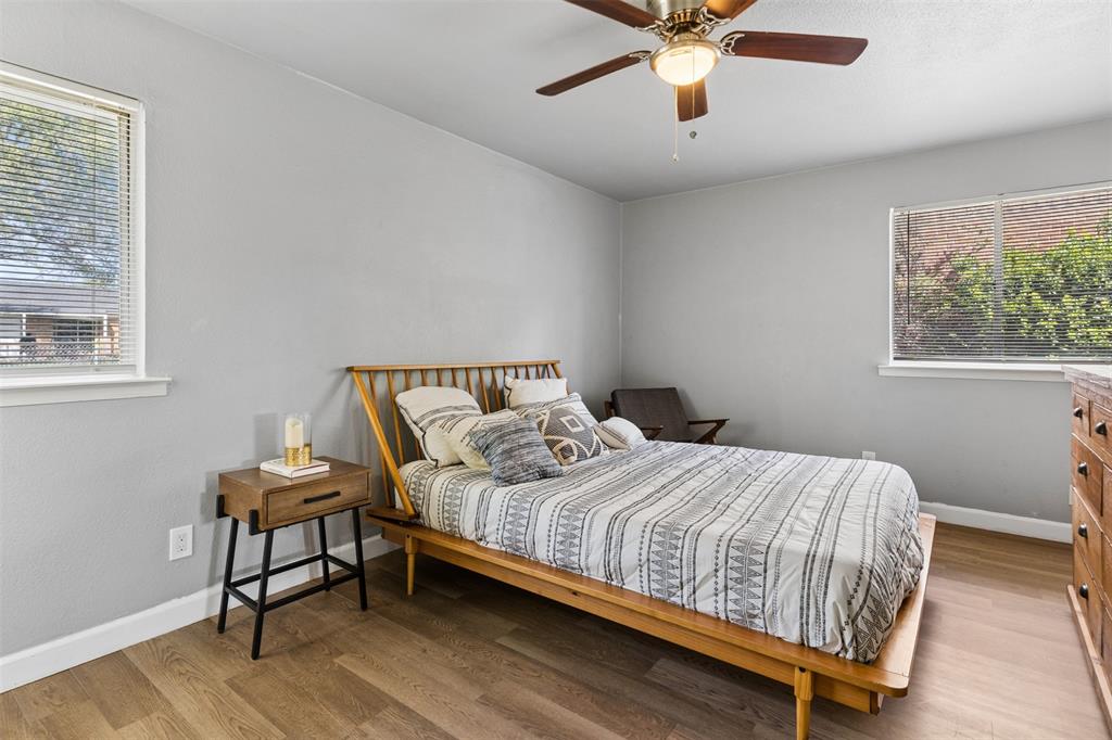 Neutral-toned interior featuring wood-finish flooring, dual windows with horizontal blinds, and a ceiling fan with integrated lighting