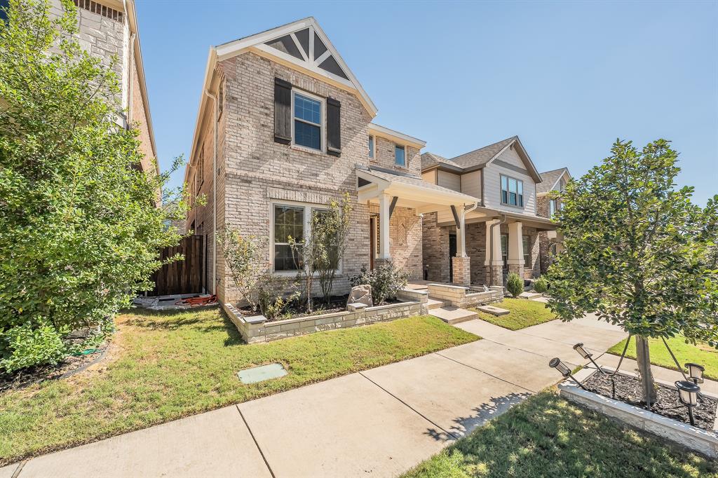 Two-story brick exterior featuring a covered front porch, stone-accented landscaping, and contrasting decorative gable trim