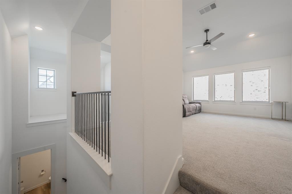 Open-concept loft area featuring a vaulted ceiling, recessed lighting, carpeted flooring, metal balustrade railing, and multiple windows, perfect for multiple uses