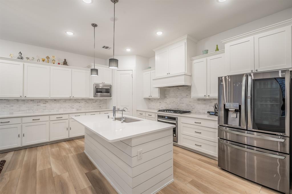 Kitchen featuring white cabinetry, wood-finish flooring, a central island with a quartz countertop, a white brick-pattern backsplash, and stainless steel appliances